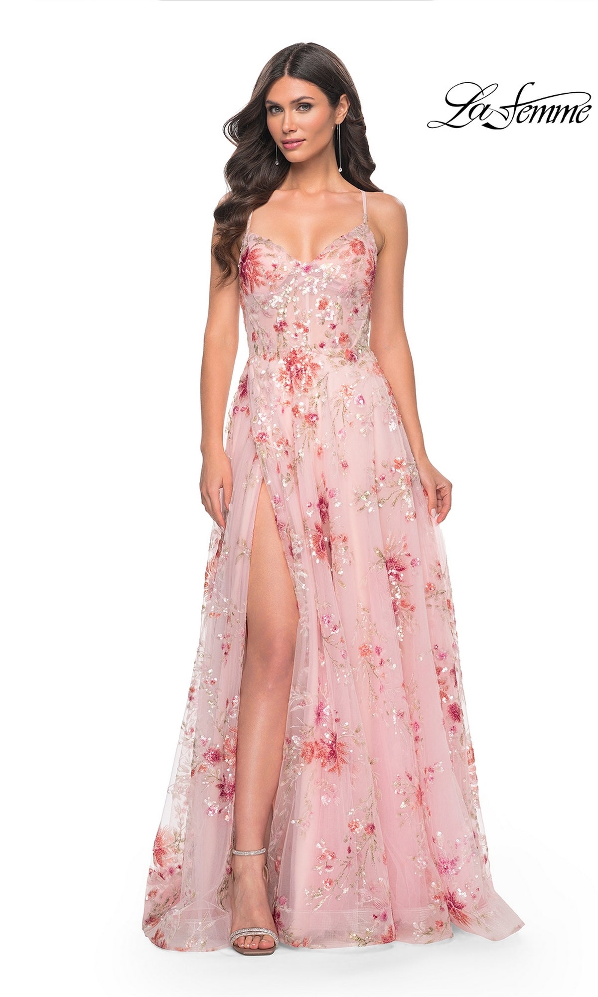 A woman wears the La Femme Floral-Sequin Long A-Line Prom Dress 32031, featuring pink floral sequins and a thigh-high slit, standing against a white background with the